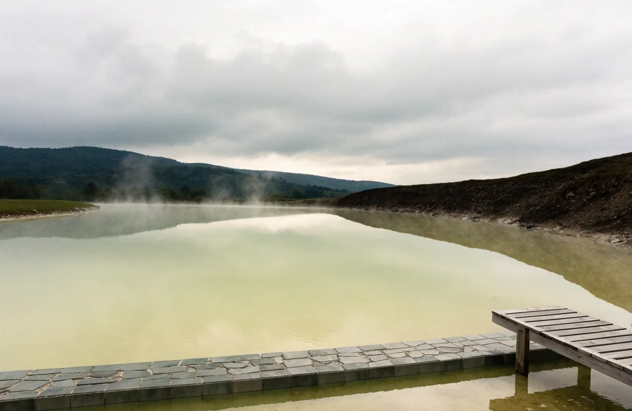 A quiet thermal basin in Slovenia at eight in the morning, still water and thin steam under flat overcast light